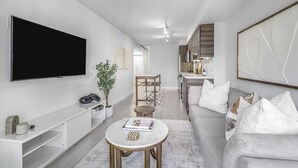 Ein modernes Wohnzimmer mit Flachbildfernseher, einer Couch, einem Couchtisch und einem Essbereich mit Stühlen.
