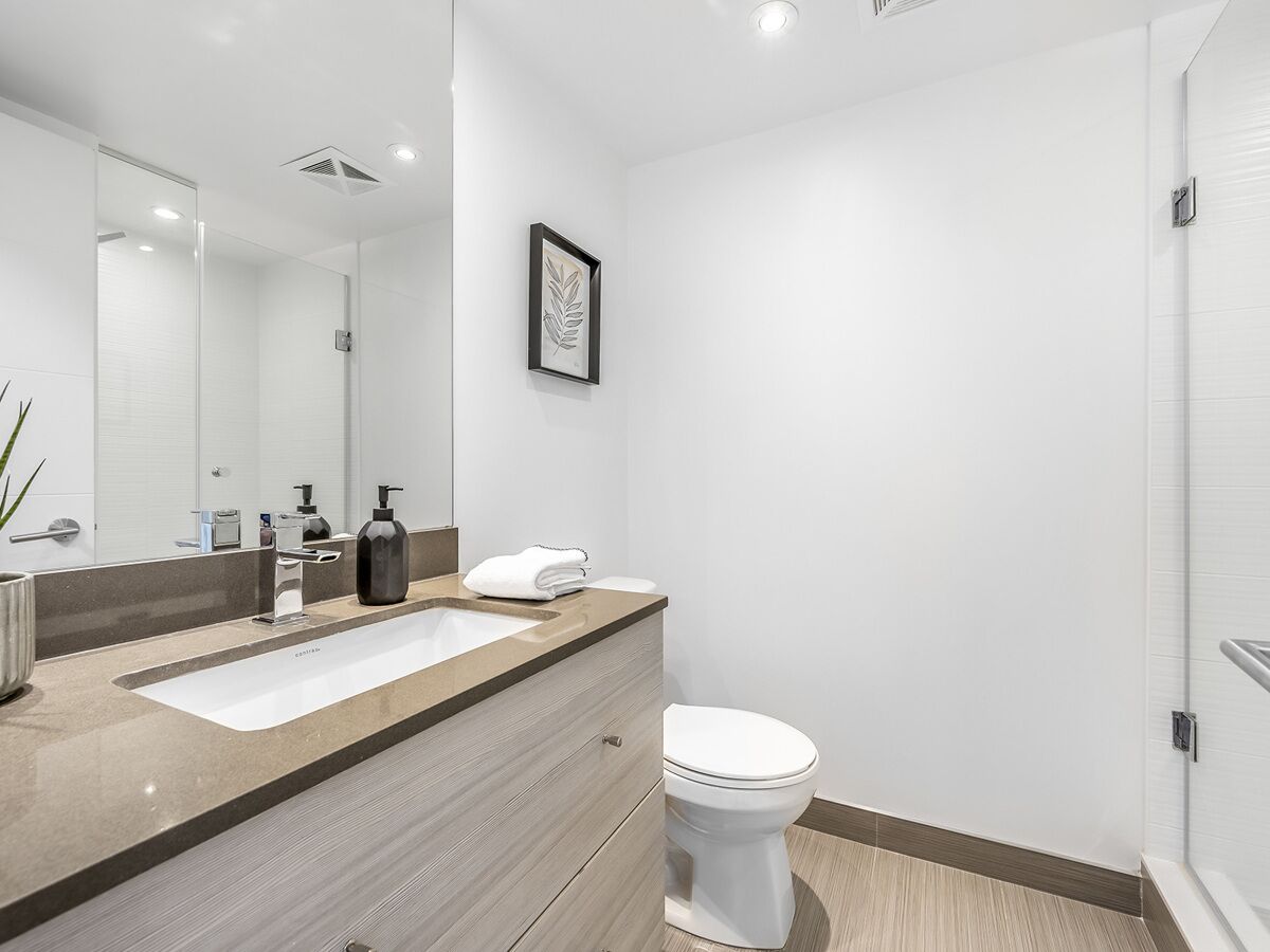 Un baño moderno con un espejo grande, dos lavamanos, un inodoro y una obra de arte enmarcada en la pared.