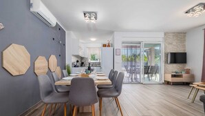 Ein modernes Esszimmer mit einem Holztisch und -stühlen, im Hintergrund eine Küche und ein an der Wand befestigter Fernseher.