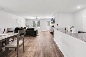 A modern kitchen with a countertop, a dining area with a table and chairs, and a living area with a sofa.