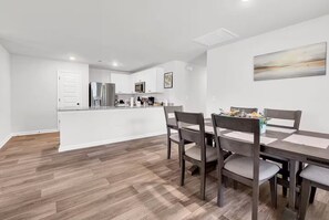 A modern kitchen with white cabinets, stainless steel appliances, and a dining area with a wooden table and chairs.