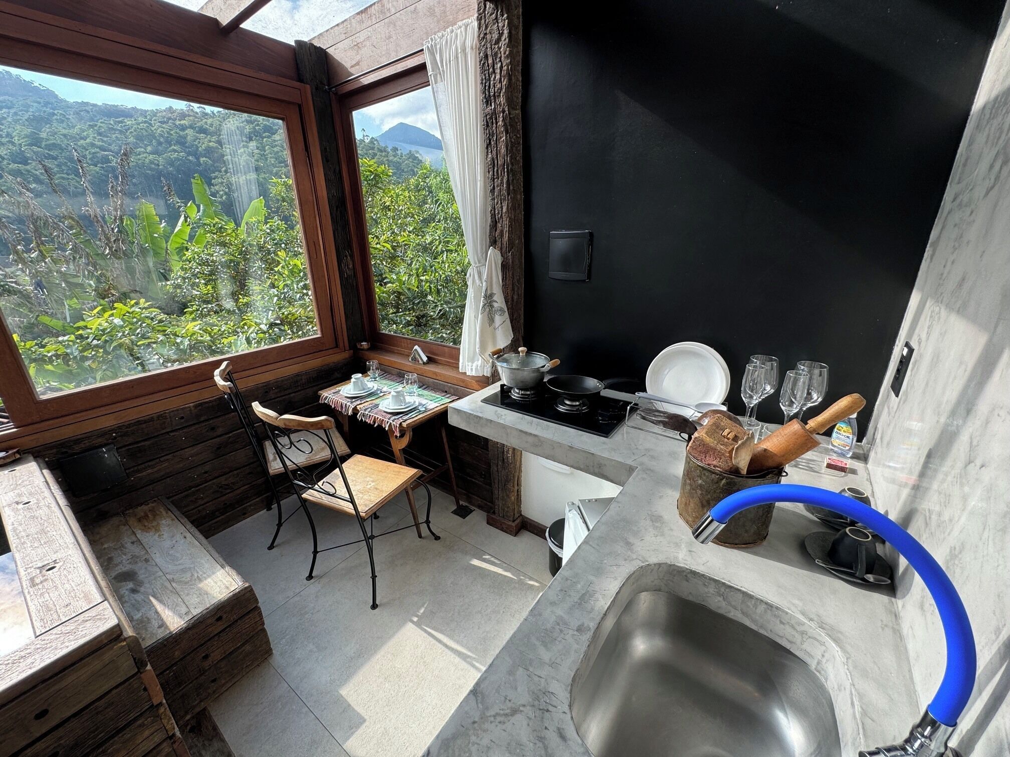 Een compacte keuken met uitzicht op een weelderig landschap, een eettafel met stoelen en een spoelbak.