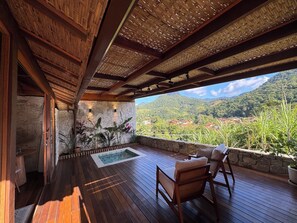 Una terraza de madera con un muro de piedra, una piscina y vistas a un paisaje montañoso.