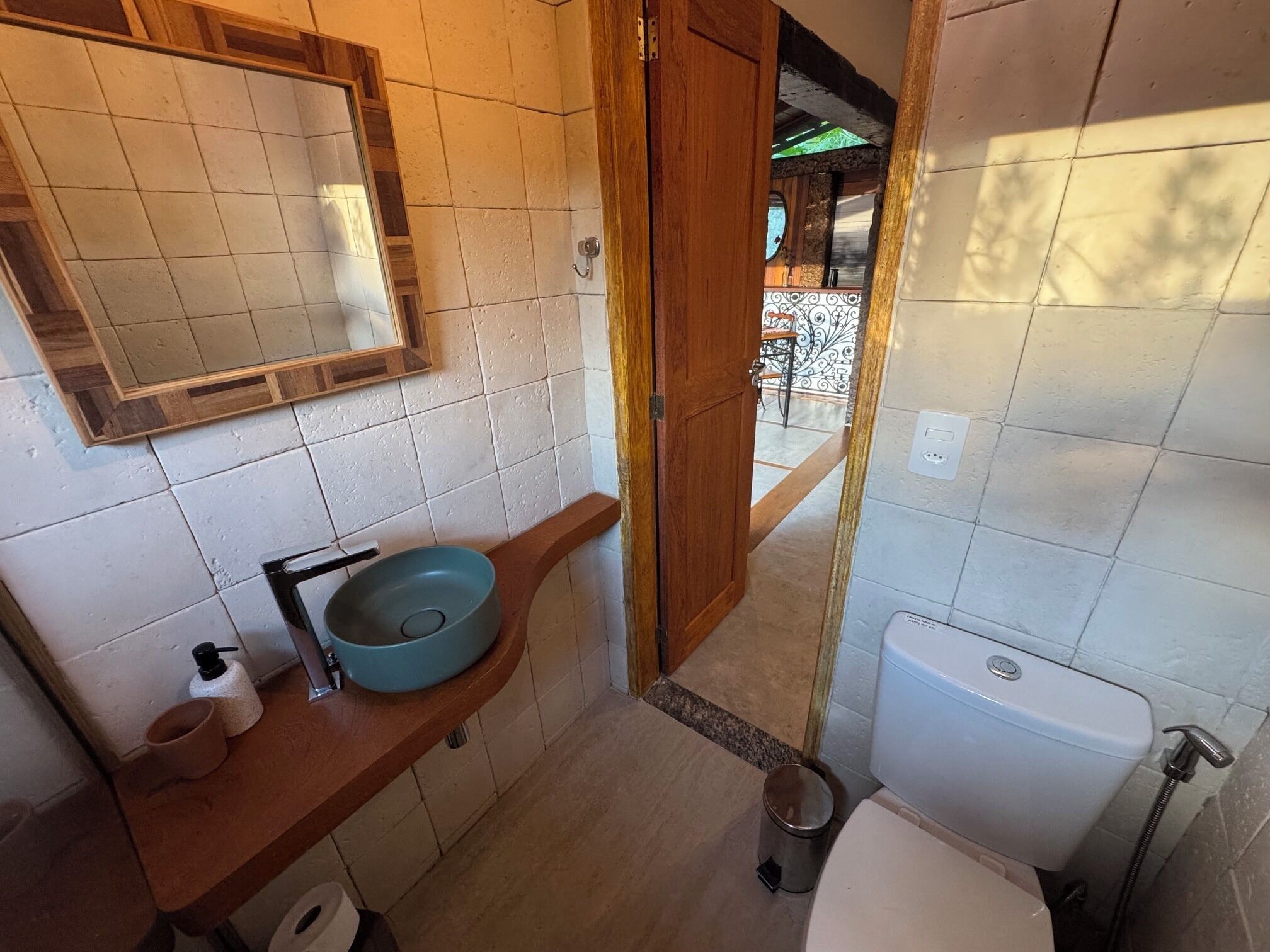Un baño con tocador de madera, un lavamanos redondo, inodoro y espejo.