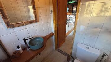 Un baño con tocador de madera, un lavamanos redondo, inodoro y espejo.