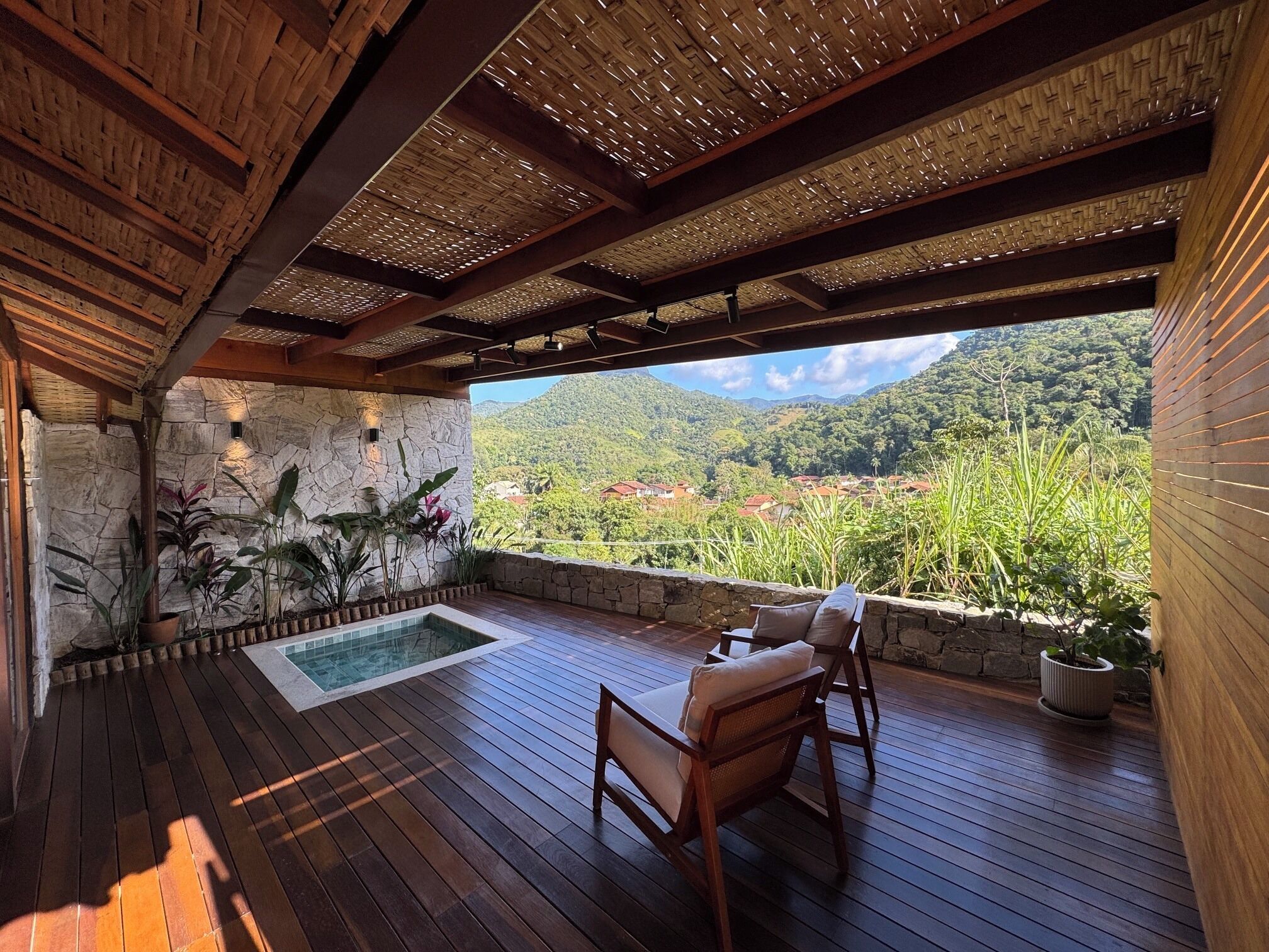 Terraza de madera con un muro de piedra, una piscina y vistas a un paisaje montañoso.