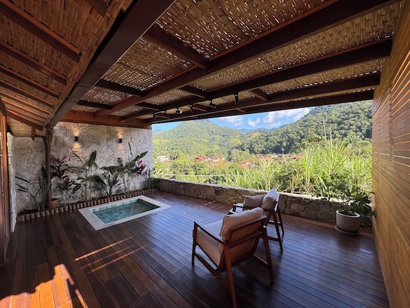 A wooden deck with a stone wall, a pool, and a view of a mountainous landscape.