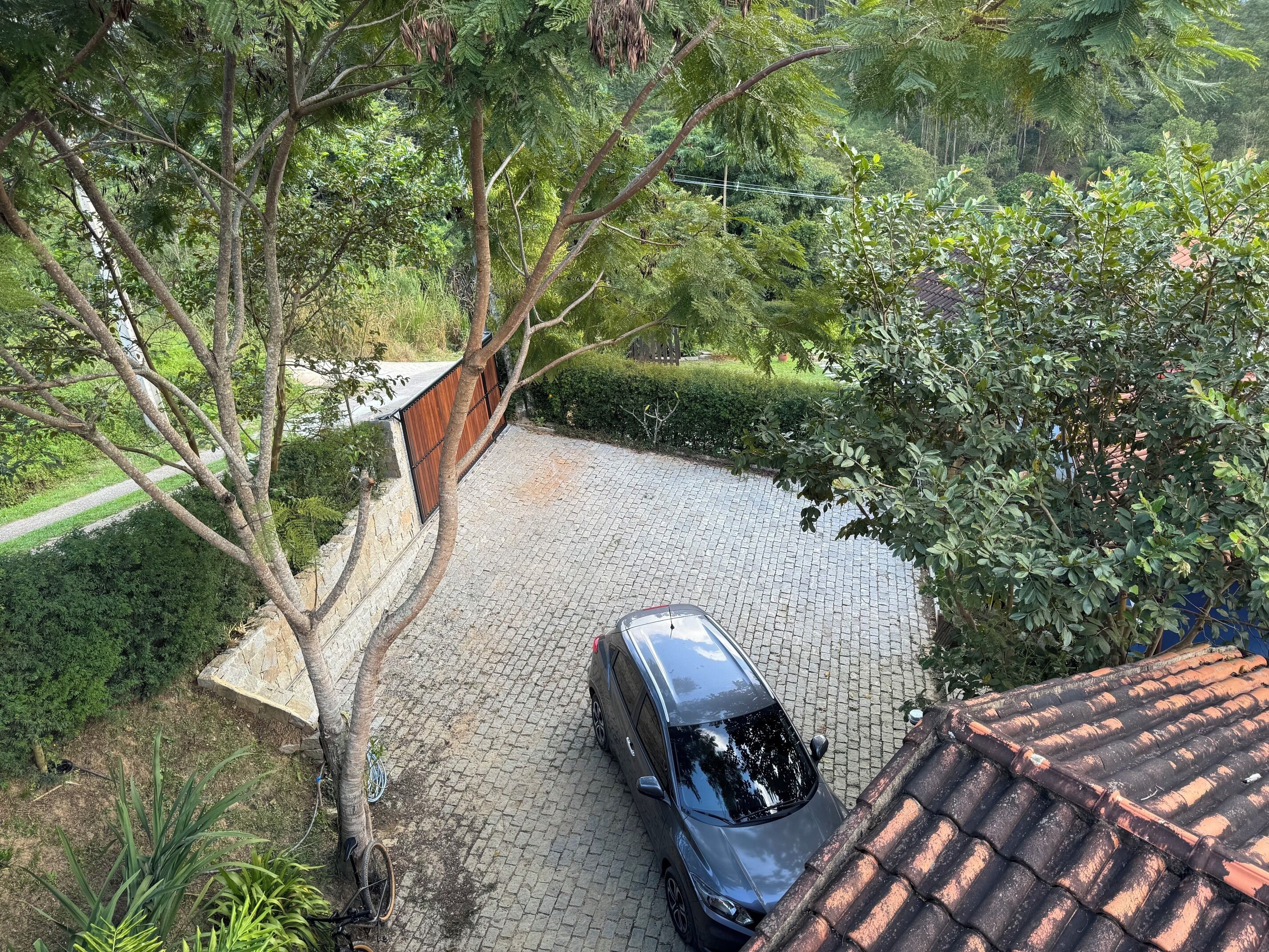 Um carro estacionado em um caminho de acesso pavimentado, cercado por vegetação exuberante e árvores.