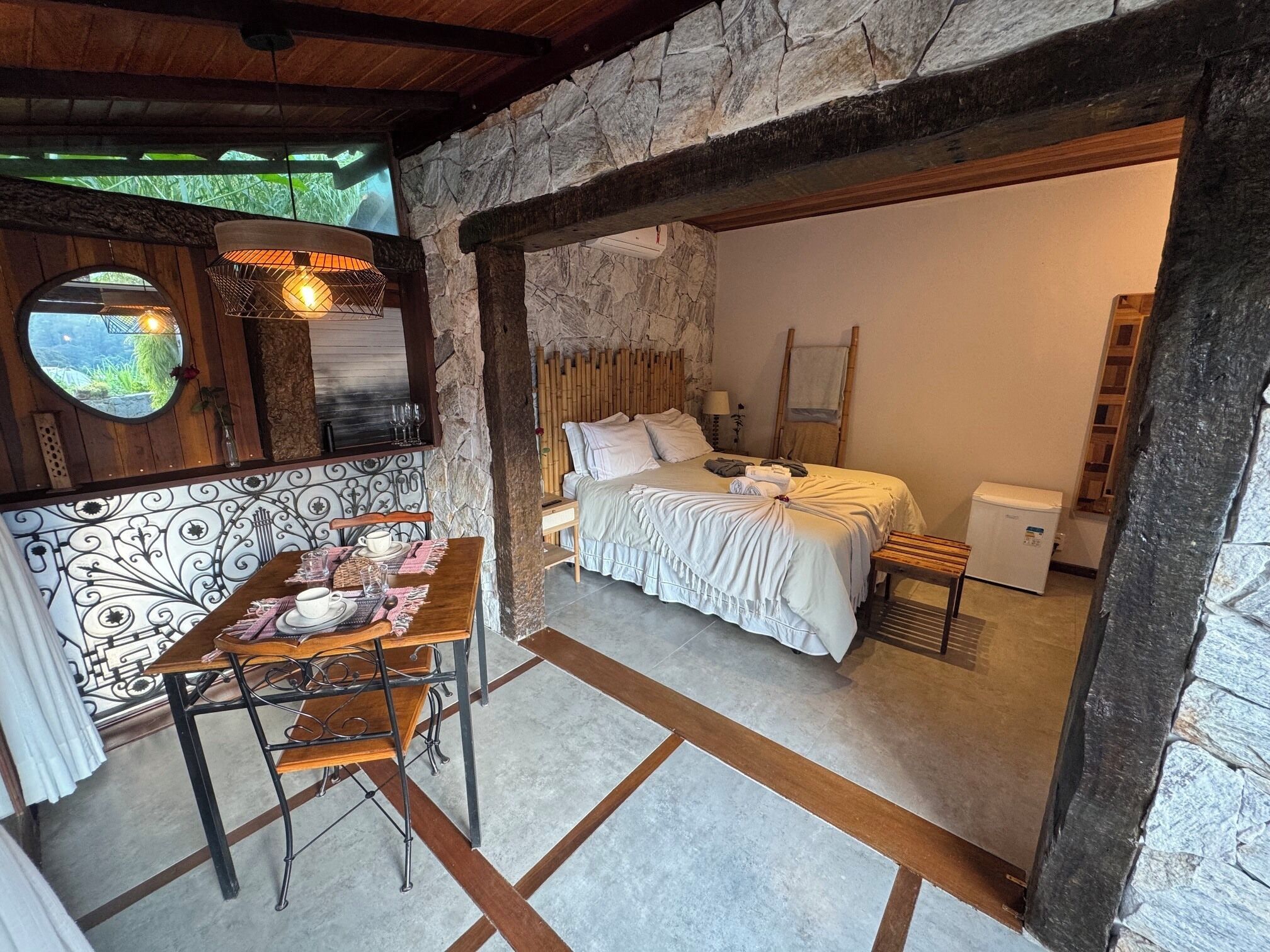 Une pièce comprenant un lit, une petite table avec des chaises, un miroir et une fenêtre donnant sur un paysage verdoyant.