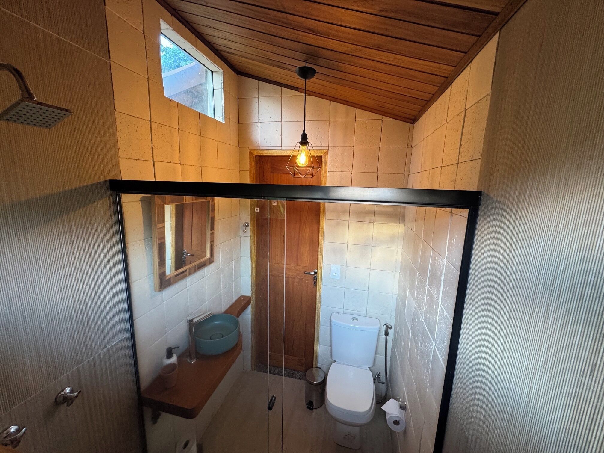 A compact bathroom with a wooden ceiling, a small window, a mirror, a toilet, and a sink.