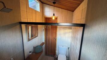 A compact bathroom with a wooden ceiling, a small window, a mirror, a toilet, and a sink.