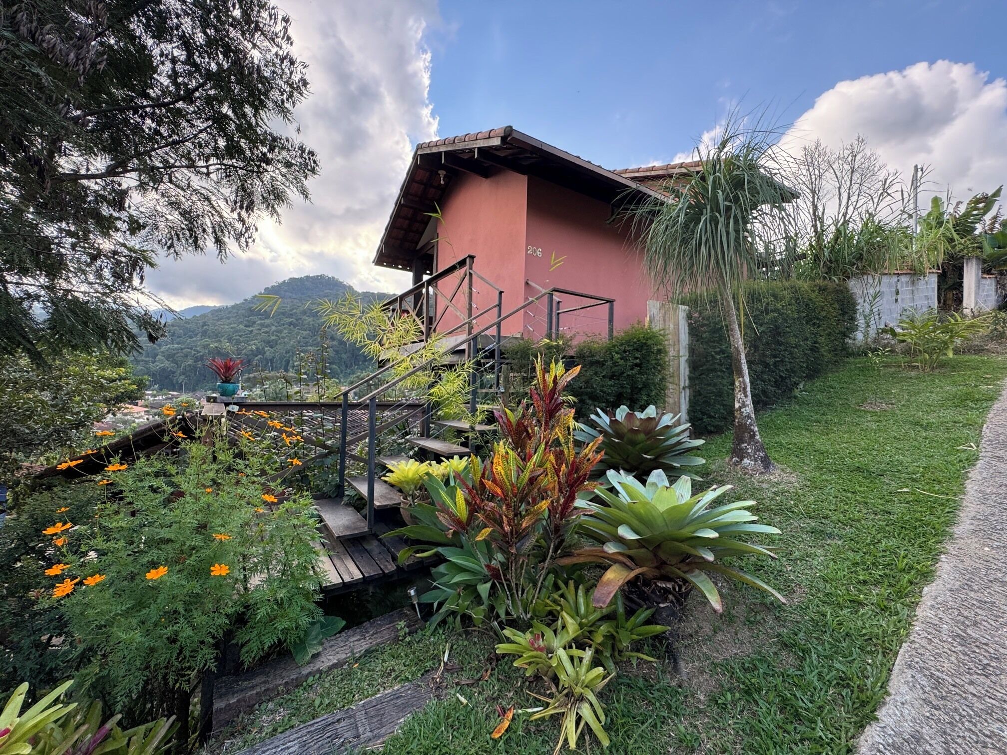 Uma casa com fachada vermelha, rodeada por um jardim com diversas plantas e flores.