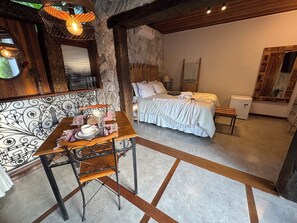Una habitación de hotel acogedora con cama, una mesa de comedor con sillas, un espejo decorativo y una pared de piedra.