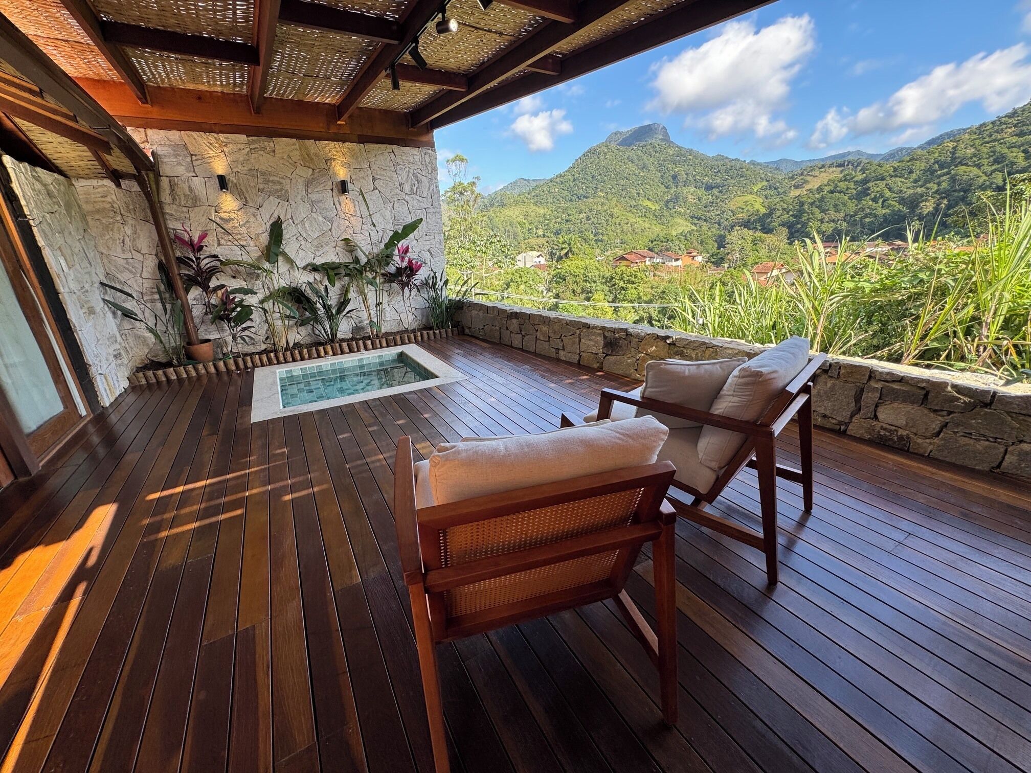 Um deck de madeira com hidromassagem, paredes de pedra e vista para uma paisagem montanhosa.