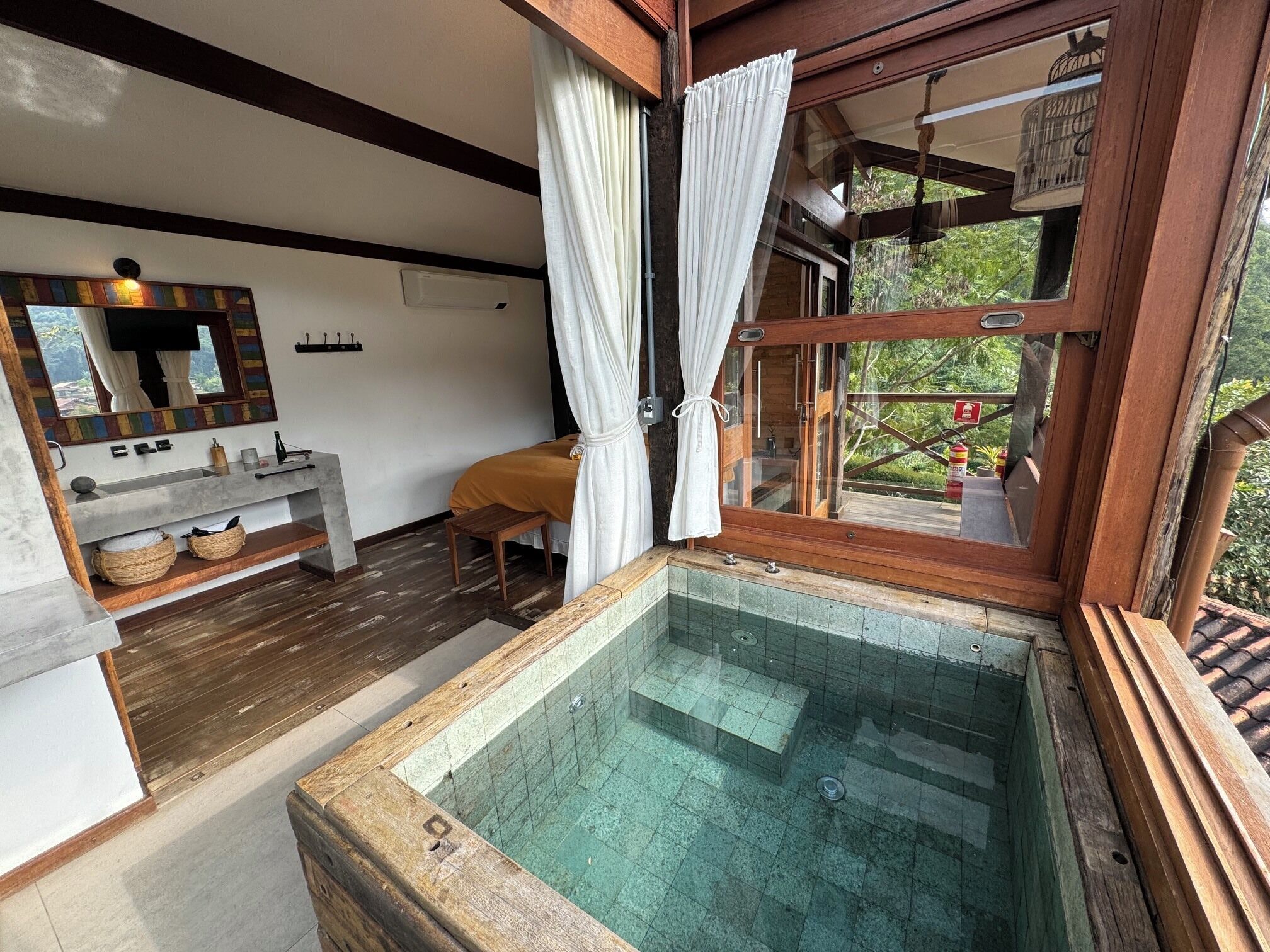 Une salle de bain avec une baignoire en bois, un banc en bois, un miroir et une fenêtre avec des rideaux.