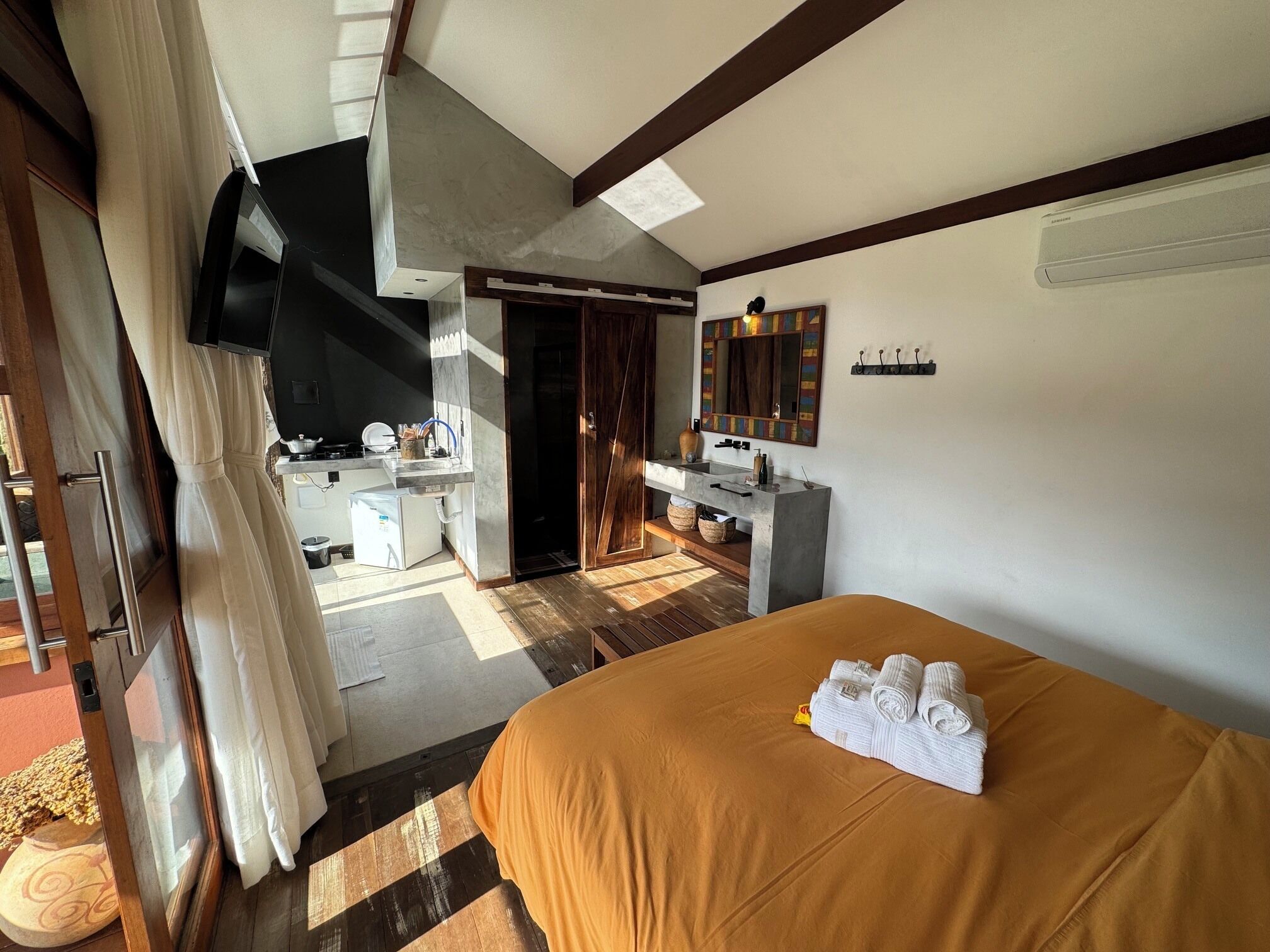 Quarto de hotel com cama, escrivaninha, espelho e banheiro.