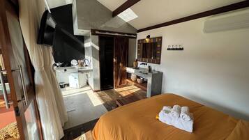 Quarto de hotel com cama, escrivaninha, espelho e banheiro.