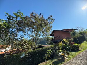 Una casa de techo rojo, rodeada de exuberante vegetación y un cielo azul despejado.