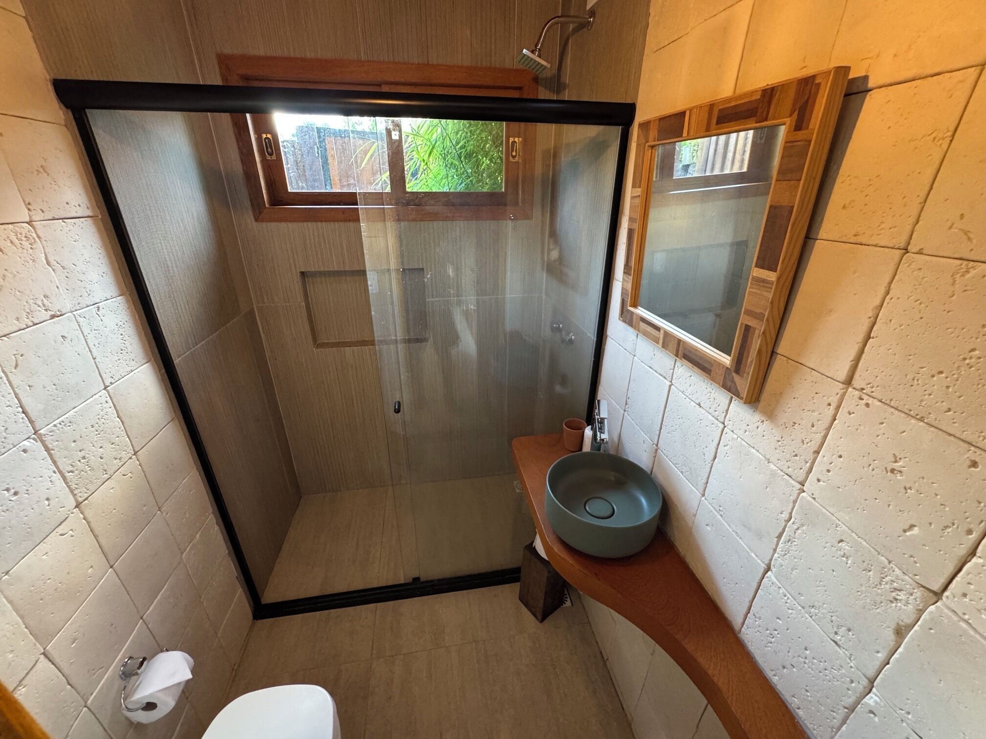 A small, enclosed shower area with a glass door, a toilet, and a sink with a bowl.