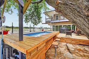 A wooden deck with a pool, stone flooring, and a view of a modern house.