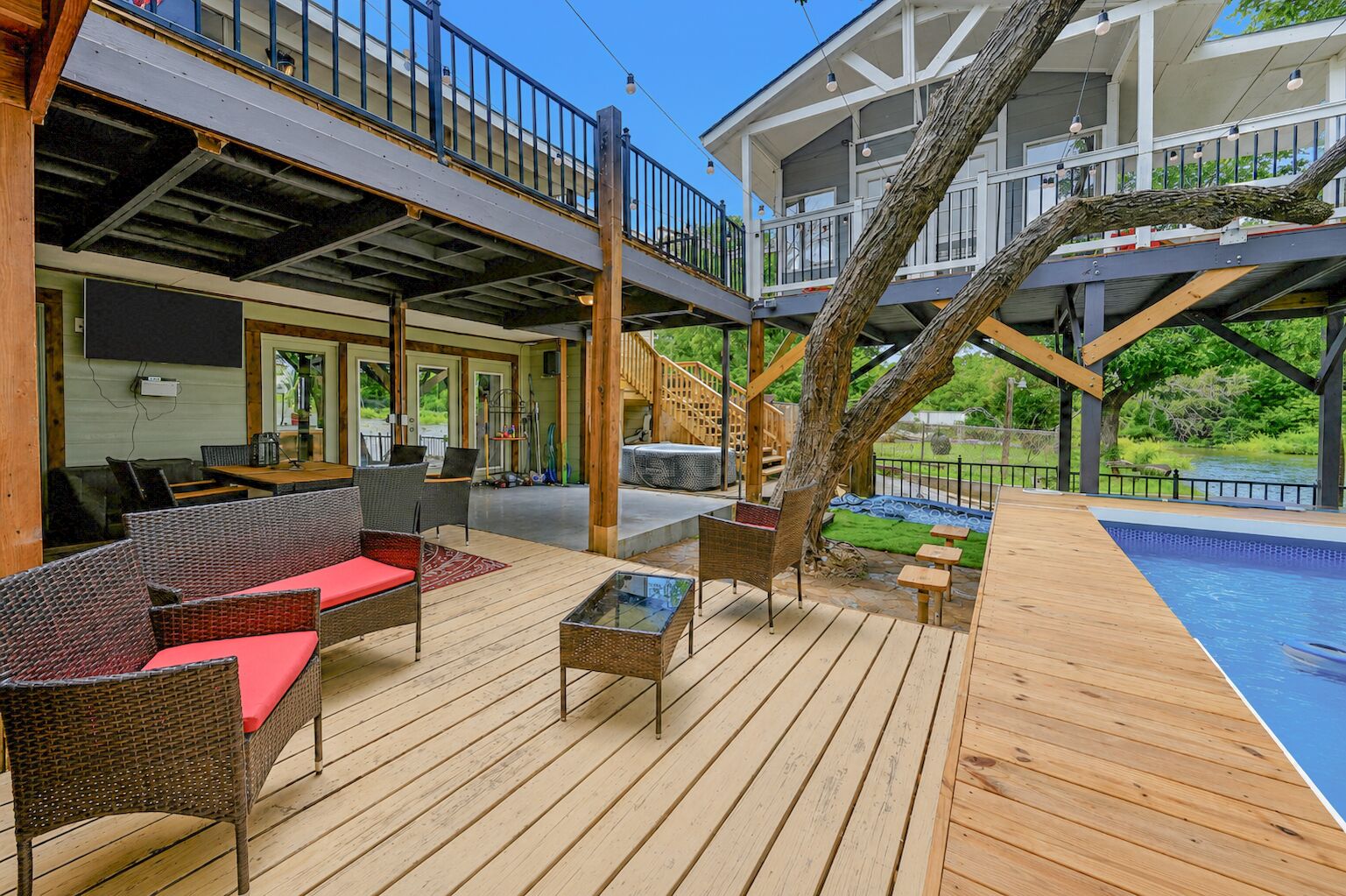 A wooden deck with outdoor furniture, a pool, and a tree.