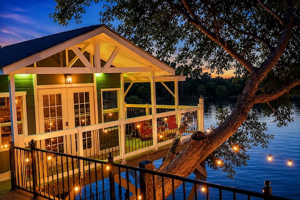A waterfront house with a deck, large windows, and string lights.