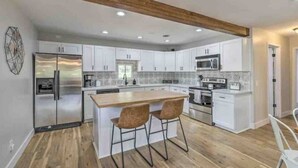 Eine moderne Küche mit weißen Schränken, einem Edelstahlkühlschrank, einer Mikrowelle und einer Holz-Kochinsel mit zwei Barhocker.