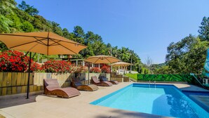 A swimming pool with lounge chairs and umbrellas, surrounded by a wooden fence and lush greenery. - Country house with heated pool, 7 bedrooms with air conditioning near São Paulo. (Juquitiba)