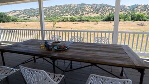 A covered outdoor dining area with a table and chairs, a bowl of fruit, and a view of a hilly landscape. - Capay Valley Country Home (Guinda)