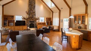 A spacious living area with a stone fireplace, wooden beams, a dining table, and a kitchen with a large island. - Capay Valley Country Home (Guinda)