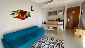 Un soggiorno moderno con un divano blu, un tappeto bianco e nero e un angolo cucina con tavolo e sedie.