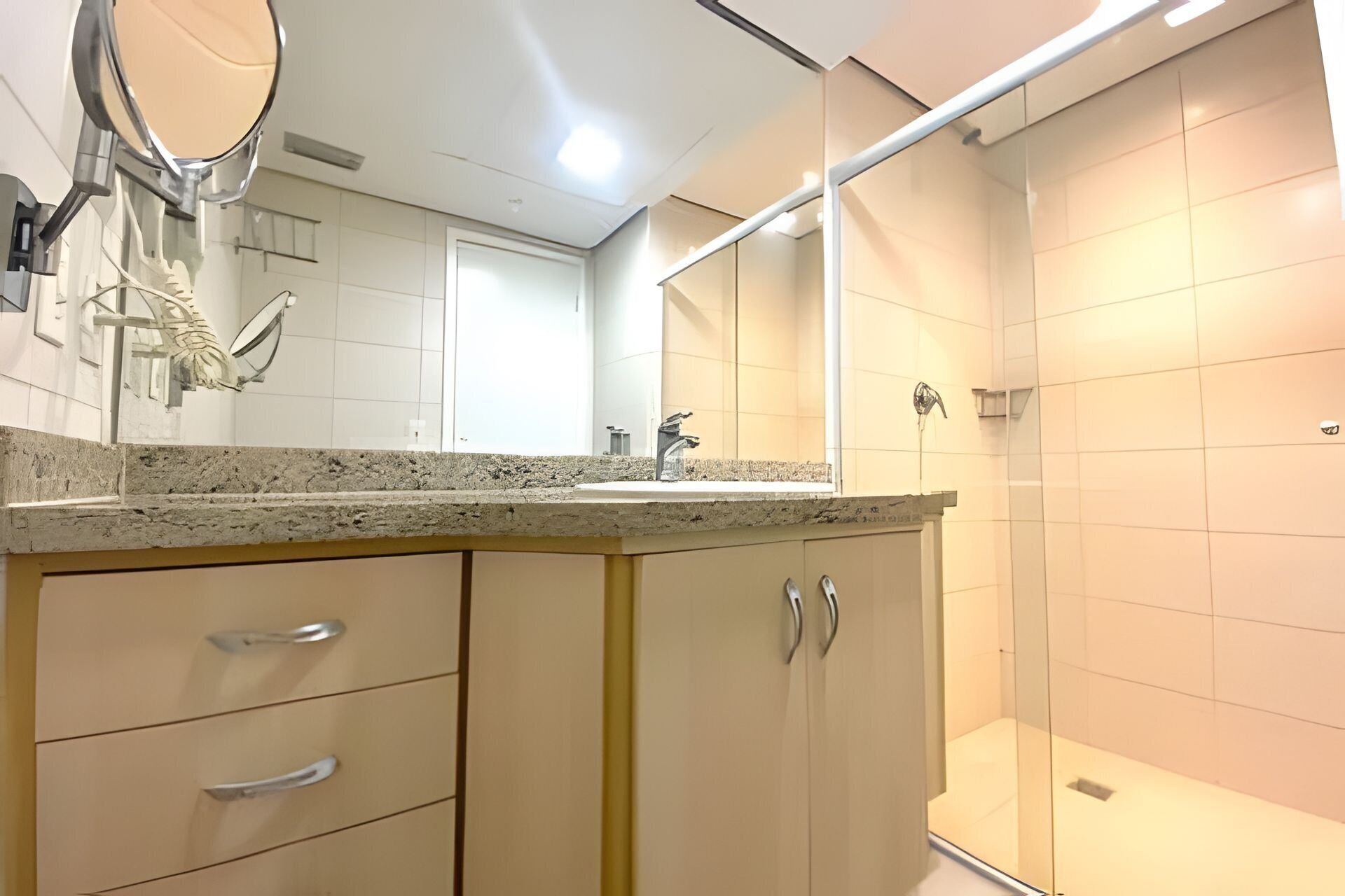 A bathroom with a granite countertop, a sink, a mirror, a shower, and a cabinet with drawers.