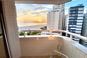 Un balcón con vistas a una puesta de sol sobre el mar, edificios cercanos y un suelo de baldosas.