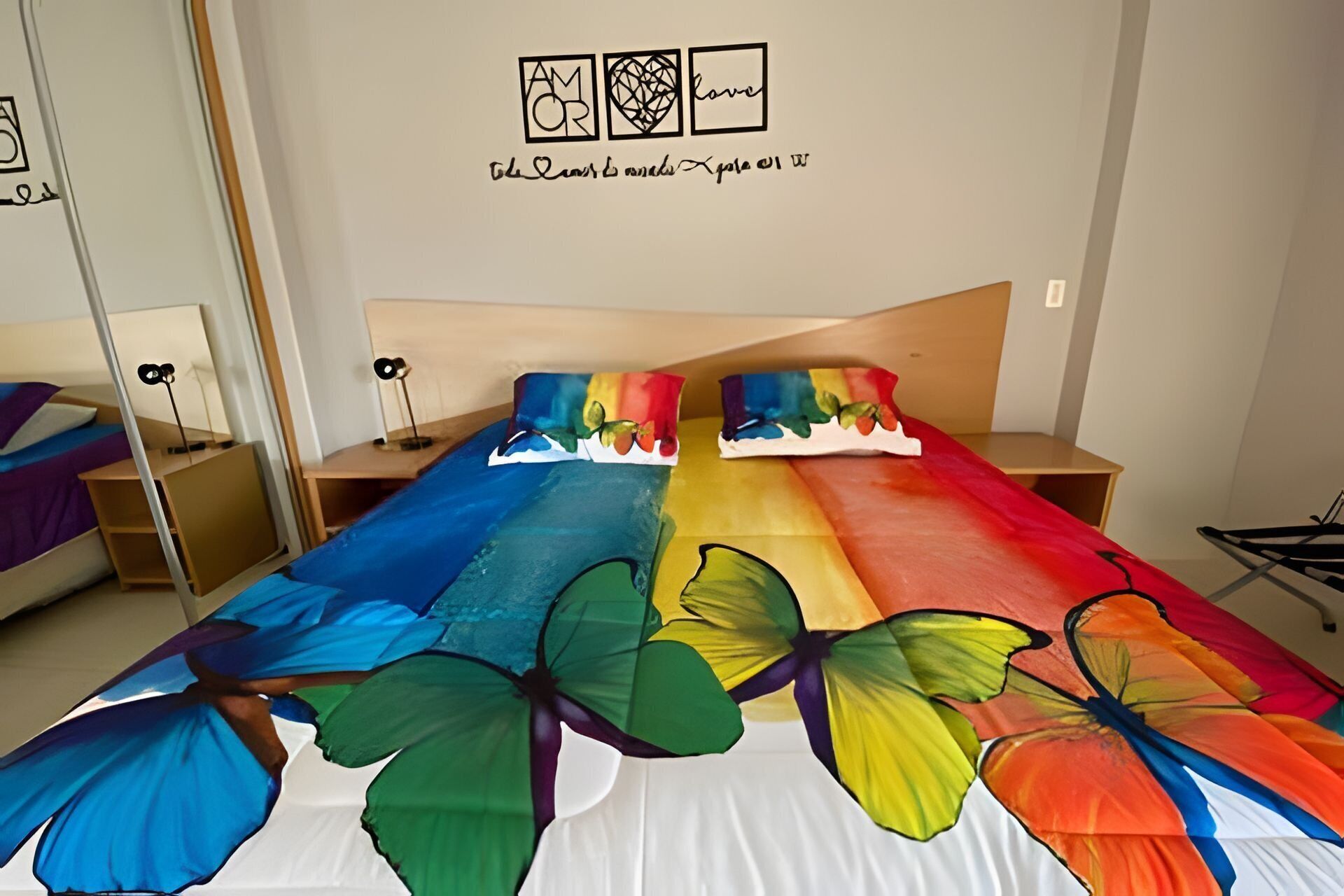 Un dormitorio con una cama cubierta de diseños de mariposas coloridas, un cabecero de madera y una pared con cuadros.