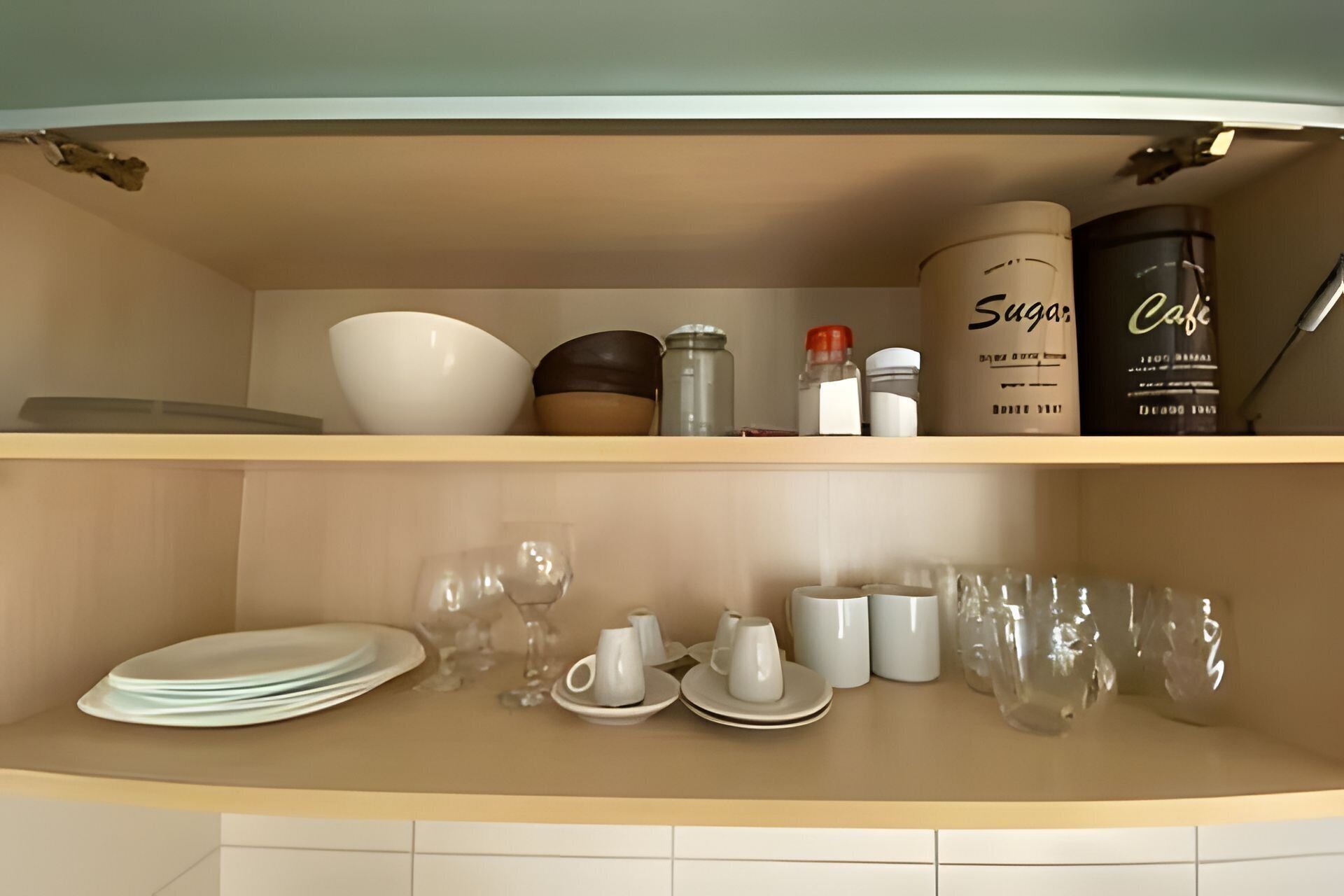 A kitchen cabinet with shelves holding various kitchenware, including bowls, cups, and containers.