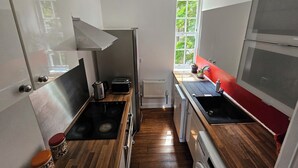 A compact kitchen with a stove, sink, and a window providing natural light. - Cosy Flat in Hammersmith - Close to tube station / But very quiet location (London)