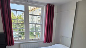A bedroom with a bed, a radiator, a window with curtains, and a view of buildings outside. - Cosy Flat in Hammersmith - Close to tube station / But very quiet location (London)