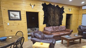 A wooden interior with a leather sofa, a dining table with chairs, and a fur rug. - Peaceful 2-bedroom cabin with AC in charming Irons, hot tub, sauna, covered deck (Irons)