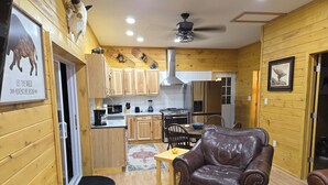 A wooden interior with a dining area, kitchen, and a leather chair. - Peaceful 2-bedroom cabin with AC in charming Irons, hot tub, sauna, covered deck (Irons)