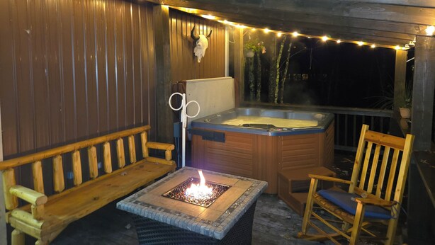 A wooden deck with a hot tub, a bench, and a chair. - Peaceful 2-bedroom cabin with AC in charming Irons, hot tub, sauna, covered deck (Irons)