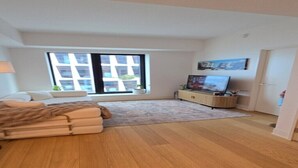 Un salon moderne avec un canapé, un téléviseur, une grande fenêtre et un plancher en bois.