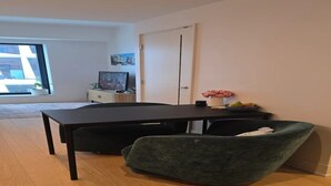 Un salon moderne avec une table en bois foncé, un fauteuil vert, un meuble blanc et une porte.