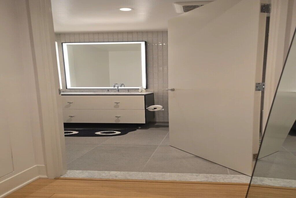 A modern bathroom with a large mirror, a sink, and a toilet.