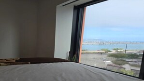 Une chambre avec un lit, une fenêtre donnant sur un paysage urbain et sur l’eau.