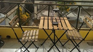 Une terrasse sur le toit, avec une table et des chaises en bois, une rambarde en métal et une vue sur les bâtiments environnants et les palmiers.