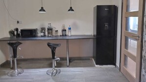 Une cuisine équipée d’un réfrigérateur, d’un four à micro-ondes, d’une machine à café et de deux tabourets de bar.
