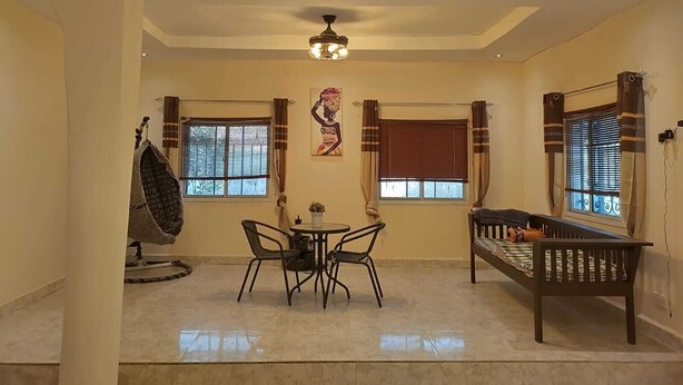 Une pièce comprenant une table à manger, deux chaises, un canapé, un ventilateur de plafond et deux fenêtres avec des rideaux.