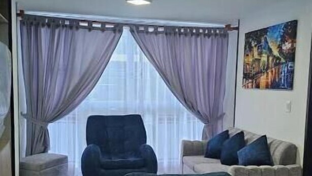 Un salon avec un canapé, un fauteuil et une grande fenêtre avec des rideaux.