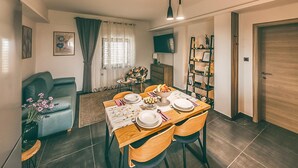 A dining area with a table set for four, a sofa, a TV, and a bookshelf.