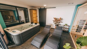 A modern bathroom with a large bathtub, a shower area, and a seating area with cushions.